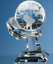 Load image into Gallery viewer, A clear crystal globe trophy on a matching faceted crystal pedestal, with the continents of South America and North America etched on the sphere, set against a solid blue background.
