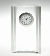 A clear glass desk clock with a cylindrical, faceted transparent body and a circular silver-rimmed clock face featuring black Roman numerals and hands.