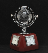 Load image into Gallery viewer, A decorative desk clock with a polished silver globe on a rotating arm mounted over a dark red octagonal base. The base features two analog clock faces with silver bezels, photographed against a solid black background.
