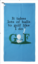 Load image into Gallery viewer, A light blue golf-themed towel featuring the embroidered text 'It takes lots of balls to golf like I do' above a green golf flag design with a white golf ball and club.
